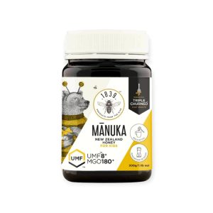 Staklena tegla Manuka meda UMF 8+ sa kremastom teksturom, postavljena na drvenoj površini uz kašičicu meda i dečiji doručak.